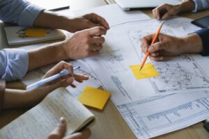 Close-up of hands working on business plans with sticky notes and drawings in an office.